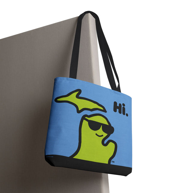 Closeup of a Michigan tote bag with a green Michigan-shaped character wearing sunglasses and smiling and saying "Hi" on a blue background.