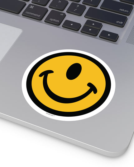 Large one-eyed smile face round sticker by the Smileclops™ brand on a laptop.