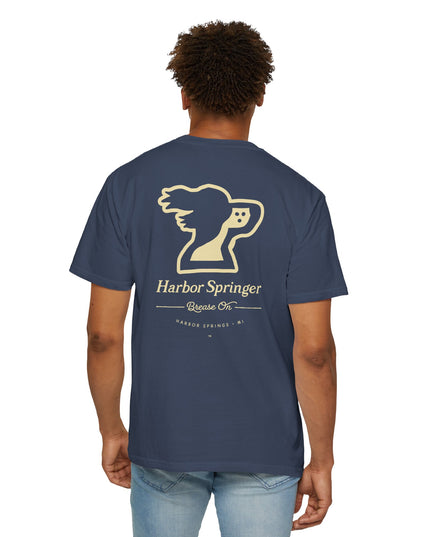 Standing man wearing a dark blue tee by the Harbor Springer brand with a springer spaniel dog logo and Brease On tagline on the back.