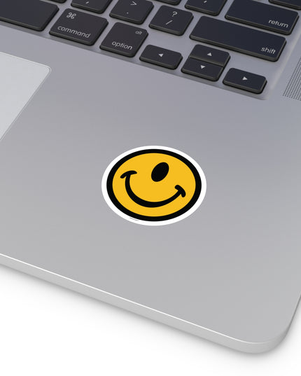 One eyed smile face round sticker by the Smileclops™ brand on a laptop.