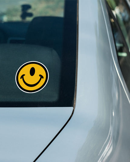 One-eyed smile face sticker that is indoor or outdoor on a car window by the Smileclops brand.