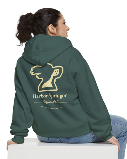 Woman sitting and wearing a green hoodie by the Harbor Springer brand with a springer spaniel dog logo and Brease On tagline on the back.