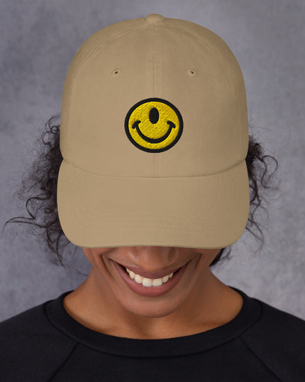 Woman wearing dad hat with the Smileclops™ brand logo of a one-eyed smile face, the official logo of resilient positivity for those who remain, in all things, Oddly Happy™.