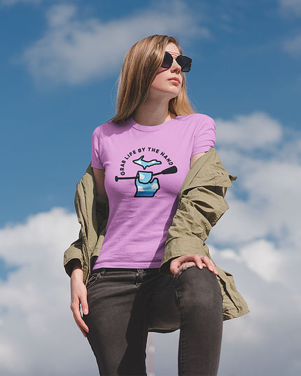 Woman wearing a pink Michigan tee that is for people who like kayaking, canoeing or paddleboarding, showing the state of Michigan grabbing a paddle with the slogan Grab Life by the Hand™.