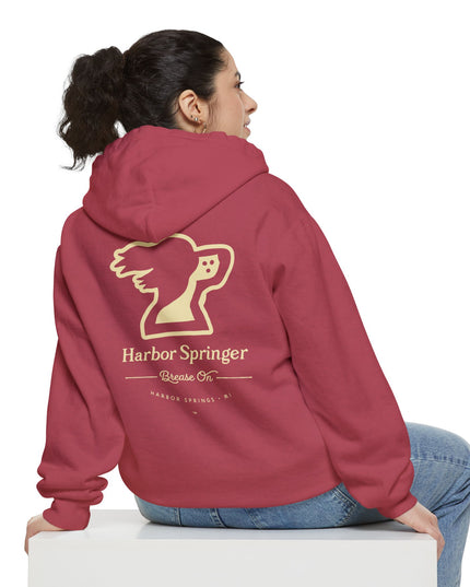 Woman sitting and wearing a red hoodie by the Harbor Springer brand with a springer spaniel dog logo and Brease On tagline on the back.