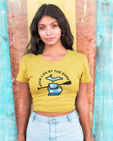 Woman wearing a yellow Michigan t-shirt for people who kayak, canoe or paddleboard, showing the state of Michigan holding a paddle with the slogan Grab Life by the Hand™.